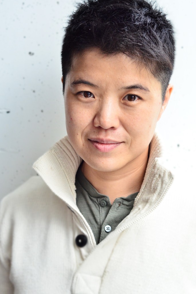 a chest-up portrait of an Asian person with a medium gold skin tone and short nearly cropped black hair. 